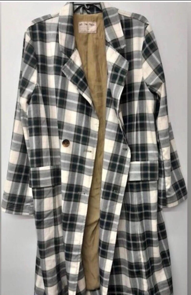 May include: A long, plaid coat in a black, white, and green pattern. The coat has a notched collar, two front pockets, and a single-button closure. The interior lining is a tan color.