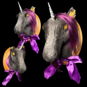 May include: Three black unicorn heads mounted on wooden plaques with purple ribbons. The unicorns have yellow and white horns and purple manes.