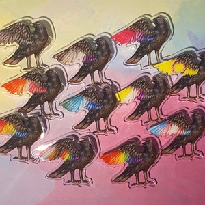 Puede incluir: Un conjunto de pegatinas con forma de cuervo. Cada pegatina presenta un cuervo negro con las alas extendidas, con un degradado arco&iacute;ris. Las pegatinas est&aacute;n dispuestas sobre un fondo degradado de rosa, amarillo y morado.