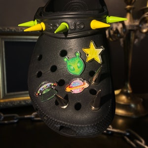May include: Black clogs with yellow spikes and colourful space-themed stickers, including an alien, a planet, and a star.
