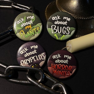 Puede incluir: Cuatro botones redondos con fondos verde, marrón y negro. Cada botón tiene texto blanco que dice "ask me about" seguido de un tema diferente: "plants", "bugs", "cryptids" y "horror movies".