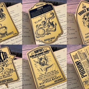 Puede incluir: Un conjunto de nueve etiquetas de estilo vintage para botellas de pociones con ilustraciones y texto. Las etiquetas están impresas en un fondo amarillo con texto negro e ilustraciones. Las etiquetas presentan nombres como "Limpiador de caldero", "Aliento de Draddy", "Agua impía", "Elixir", "Fórmula de reemplazo de sangre de vampiro", "Veneno" y "Secretos del cementerio".