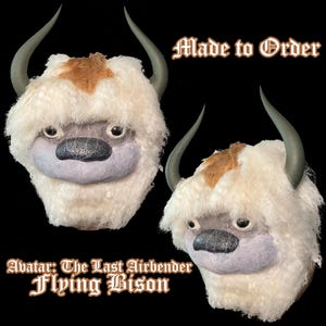 May include: Two plush Appa masks from Avatar: The Last Airbender. The masks have white fur, grey horns, and a brown patch on the head. The text "Made to Order" and "Flying Bison" are visible.