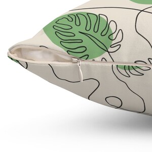 May include: A cream-colored throw pillow with a zipper closure. The pillow features a green and black abstract leaf design.