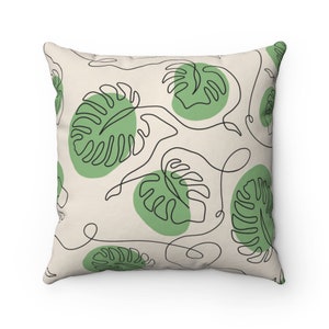 May include: A throw pillow with a cream-colored background and a repeating pattern of green monstera leaves outlined in black. The leaves are stylized with a single line drawing.