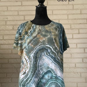 May include: A green, blue, and white tie-dye shirt with a round neckline and short sleeves. The shirt is on a mannequin and the text "Size 2X" is visible in the image.