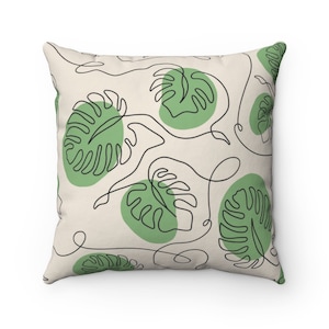 May include: A square throw pillow with a cream background and a repeating pattern of green leaves with black outlines. The leaves are stylized and resemble monstera leaves.