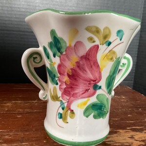 May include: White ceramic vase with two handles and a floral design. The vase is painted with pink, yellow, and green flowers.