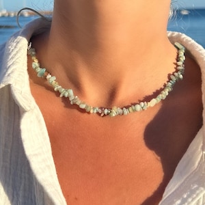 May include: A delicate necklace made of light blue and green gemstone chips. The necklace is worn by a person with a white shirt.