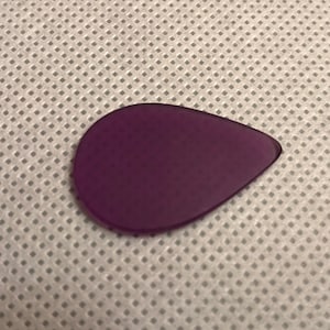 May include: A purple guitar pick with a teardrop shape.