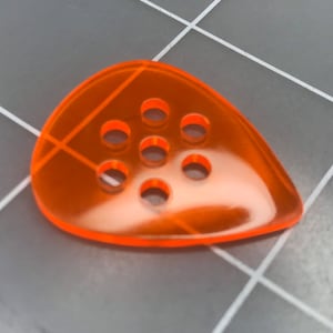May include: Orange guitar pick with a teardrop shape and multiple round holes.