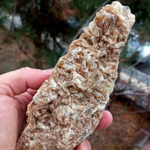 May include: A large, rough, brown rock with a cluster of small, clear, glassy crystals. The crystals are arranged in a random pattern and have a slightly iridescent sheen.