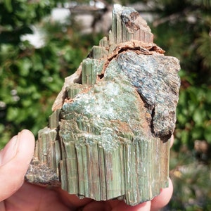 Könnte beinhalten: Ein grüner und brauner Stein mit einer geschichteten, gestreiften Textur. Der Stein hat eine raue, natürliche Oberfläche und scheint eine Art Mineralprobe zu sein.
