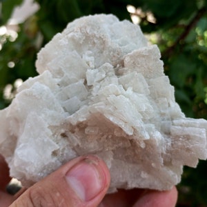 May include: A cluster of white, translucent crystals with a layered, stacked formation. The crystals have a rough, natural texture.