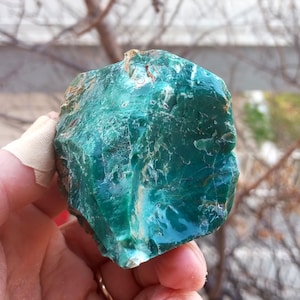 Può includere: Una grande gemma verde ruvida con una finitura traslucida e vetrosa. La pietra ha un aspetto screziato con striature verde scuro e bianche.