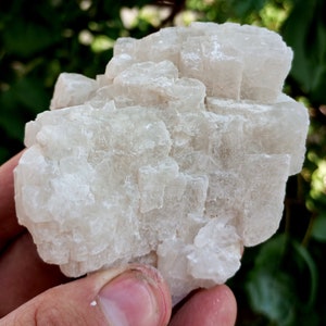 May include: A large, white, crystalline rock with a rough, textured surface. The rock is made up of many small, cubic crystals.