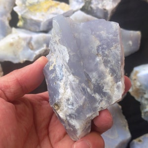May include: A large, rough piece of blue chalcedony with white and gray markings. The chalcedony is translucent and has a smooth, polished surface.