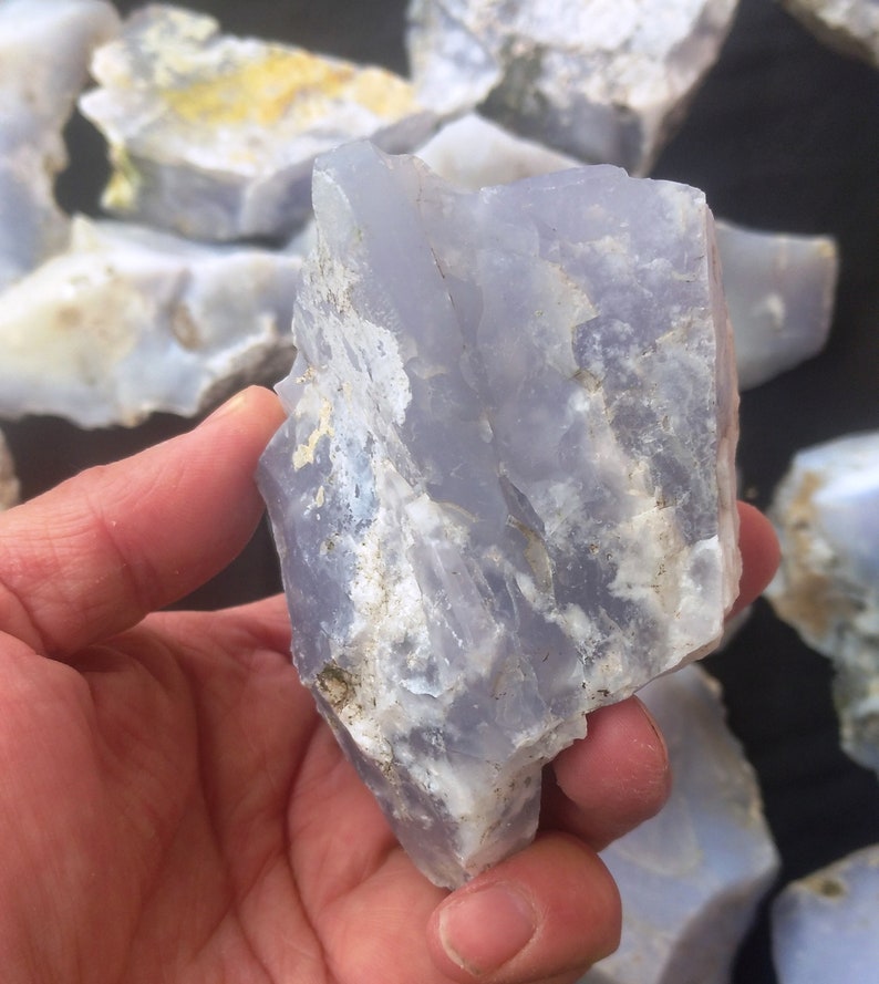 May include: A large, rough piece of blue chalcedony with white and gray markings. The chalcedony is translucent and has a smooth, polished surface.