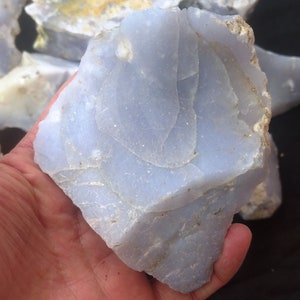 May include: A large, light blue, translucent, rough-cut piece of blue lace agate. The agate has a layered, banded pattern with white and gray inclusions.