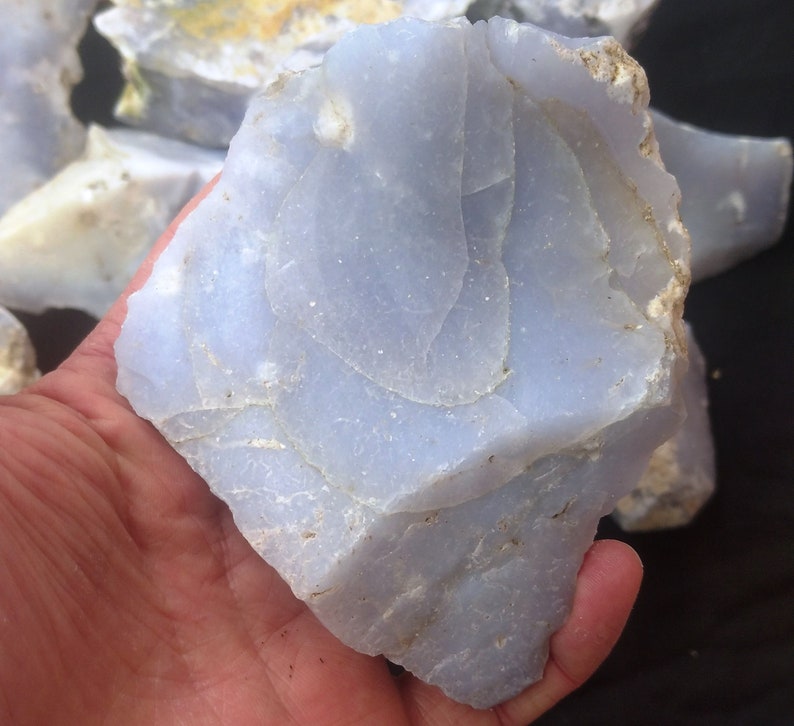 May include: A large, light blue, translucent, rough-cut piece of blue lace agate. The agate has a layered, banded pattern with white and gray inclusions.