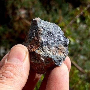 May include: A rough, gray rock with silver-colored flecks. The rock is being held in a hand.