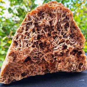 Puede incluir: Un gran espécimen mineral en forma de semicírculo que presenta una red densa e intrincada de cristales en forma de aguja de color marrón claro. La estructura es porosa y texturizada, mostrando una variedad de tonos tierra y ocre.