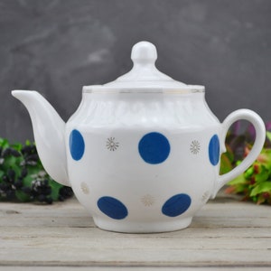 May include: White teapot with a blue and gold polka dot pattern. The teapot has a lid with a knob on top.