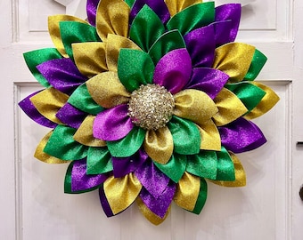 Puede incluir: Una corona de Mardi Gras con flores de papel de purpurina verde, morado y dorado. El centro de la corona tiene una bola de purpurina dorada.