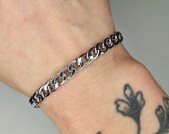 May include: A silver chain bracelet with a curb link design. The bracelet is worn on a person's wrist.