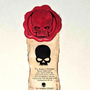 Puede incluir: Un rollo de pergamino con un sello de cera roja que presenta un diseño de calavera. El rollo contiene texto en tinta negra con un gráfico de calavera y espada en la parte inferior. El texto dice: "Sete Numquam Relinquam Amoris sumus perili Leges noseis neстоп сдо Debetionem pienam intendo Banc non habebis er ullo alio Communicare bolo tibi quod sentio Intelligendum tibi est Tete numquam relinquam tete numquam descram tibi cro desultor non numquam faciame non flere te Nec dicam valere mendar bulncrabo non numquam Te cognovi tam diu Cor tuum dolet. at timidior quin dicas Intus nos ambo scimus quid fiat Ludum callemus et nos ludemus Et si regas me quomodo sentias tie dicas te tam cacram cose Te rognobi tam diu Cor tuum dalet. at timidior qasin dicas Intus nos ambo scimus quid fiat Ludum callemus et nos ludemus Communicare bolo tibi quod sentio Intelligendum tibi cst"