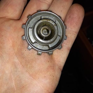 Puede incluir: Un engranaje de metal plateado con un agujero central y una serie de dientes alrededor del borde.