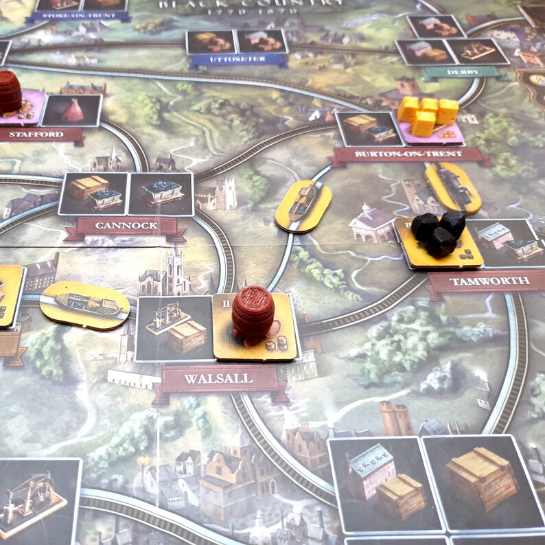 May include: A game board with a map of the Black Country in England, 1770-1870. The board features various cities and towns, including Stafford, Cannock, Walsall, Burton-on-Trent, Tamworth, and Uttoxeter. There are wooden pieces and tokens on the board, including a red barrel, a black coal token, and yellow train tokens.