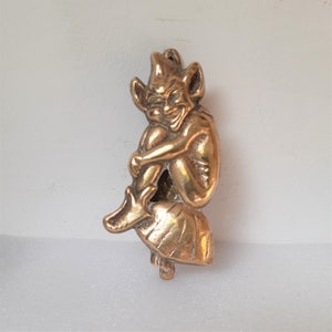May include: A brass door knocker shaped like a goblin or imp, sitting with its legs crossed. The knocker is intricately detailed and has a mischievous expression.