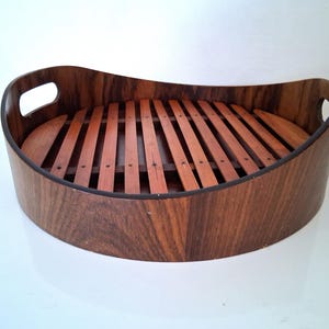 May include: A wooden serving tray with a curved shape and a slatted bottom. The tray is made of dark wood with a natural grain pattern.