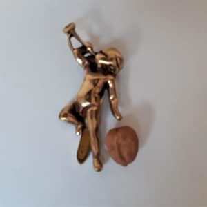 May include: A gold-coloured metal figurine of a cherub playing a trumpet. The cherub is standing on a small, flat, gold-coloured metal base.