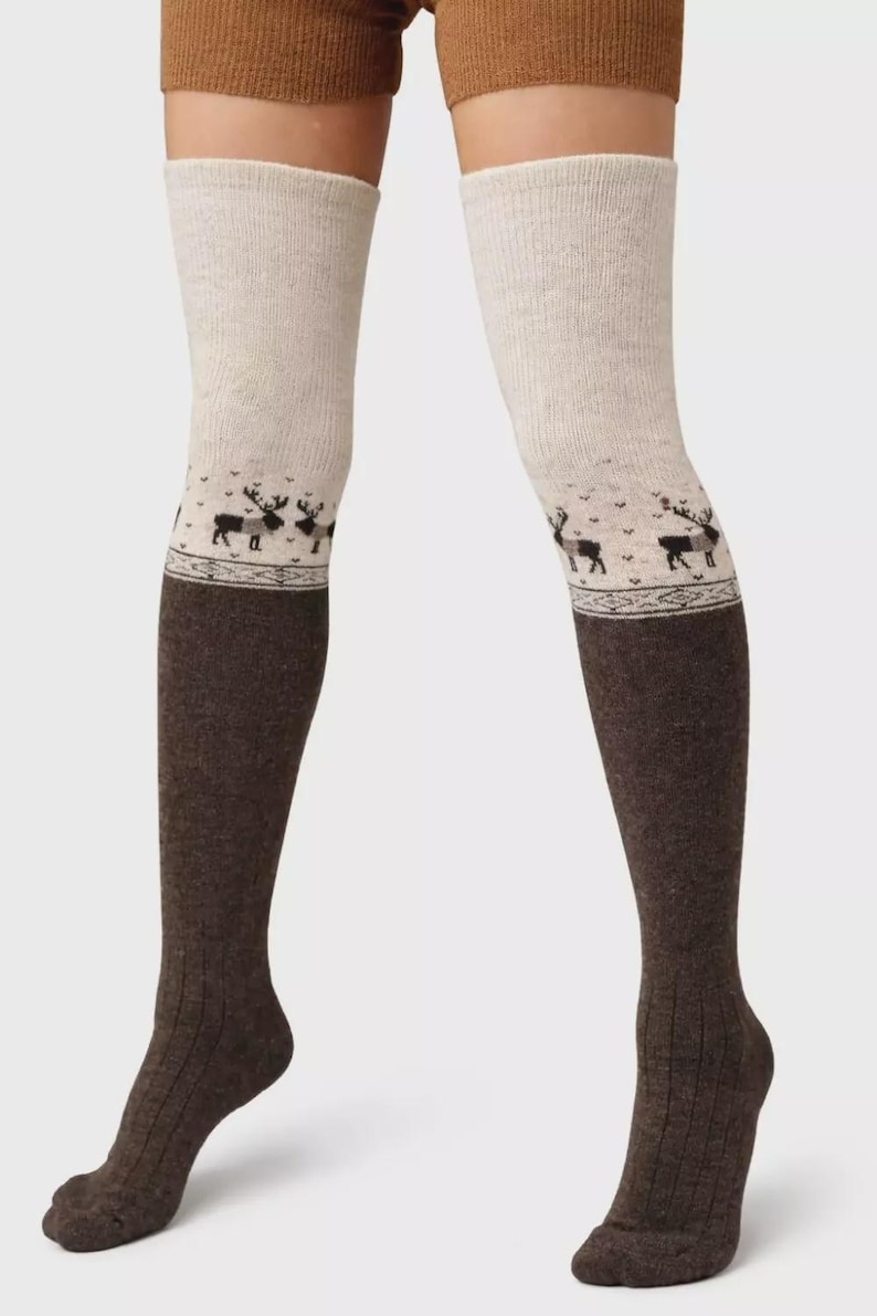 May include: Two-tone over-the-knee socks. The upper section is light beige, changing to dark brown below the knee. A decorative band featuring a reindeer pattern is at the transition. The socks have a ribbed design.
