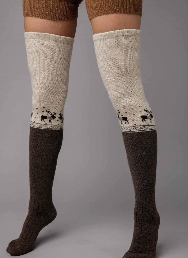 May include: Two-tone over-the-knee socks. The upper section is light beige, changing to dark brown below the knee. A band of reindeer silhouettes decorates the beige section. The socks have a ribbed texture.