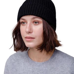 May include: A black ribbed knit beanie hat. The hat is worn by a person with short brown hair and a gray sweater. The beanie is a classic winter accessory, offering warmth and style. The hat is made of a soft, flexible material.