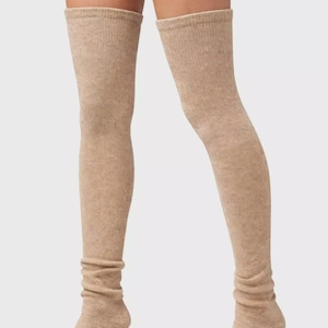 Puede incluir: Un par de calcetines beige por encima de la rodilla. Los calcetines están hechos de un material de punto acanalado suave. La parte superior de los calcetines está doblada. Los calcetines están subidos hasta la mitad del muslo. Los calcetines son de color beige.