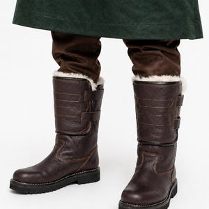 May include: Dark brown leather winter boots with a faux fur lining and adjustable straps. The boots have a robust design with a thick black sole. Suitable for cold weather. The boots are shown from the knees down.