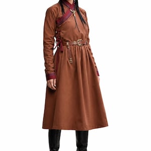 May include: A brown midi-length dress with long sleeves, a high collar, and a side-tie closure. The garment features dark red and purple striped trim along the neckline and cuffs, paired with a brown leather belt featuring a gold-toned buckle.