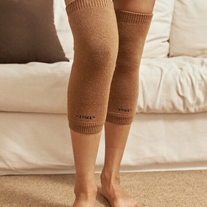 May include: A pair of brown knee-high socks with the word "TOUT" written on the left sock and "TOUT" written on the right sock.