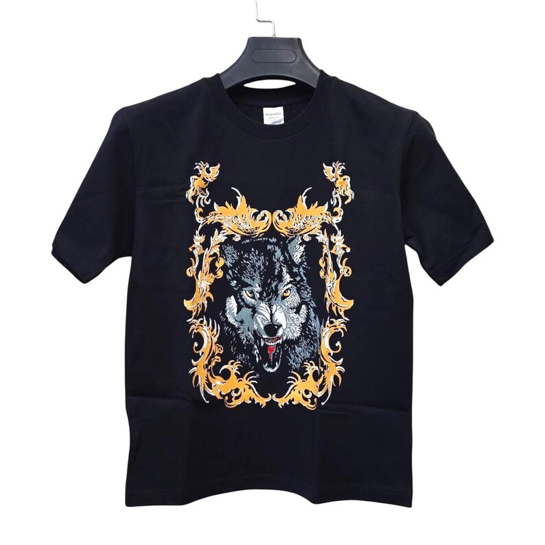 May include: Black t-shirt featuring a detailed illustration of a wolf with an open mouth, set within an ornate gold frame. The wolf's fur is rendered in shades of gray and white, with red accents on its tongue. The design is centered on the shirt.