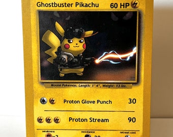 May include: A yellow Ghostbuster Pikachu Pokemon card featuring a cartoon image of Pikachu in a Ghostbuster uniform, holding a proton pack. The card has a yellow background with black text and a black border. The card's text includes the Pokemon's name, type, HP, attacks, weakness, resistance, and retreat cost.