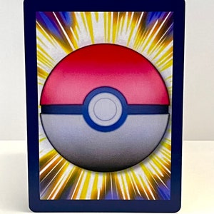 May include: A close-up of a Pokemon trading card with a blue border and a white and red Pok&eacute; Ball in the centre. The Pok&eacute; Ball is surrounded by a yellow starburst.