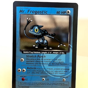 May include: A blue and black Mr. Frogastic Pokemon card with a picture of a blue frog with yellow eyes. The card has a white border and black text. The text on the card reads "Basic Pokemon", "Mr. Frogastic", "90 HP", "Bubble Frog Pokemon", "Length: 2'0", "Weight: 24 lbs", "Stretch Punch", "This attack does 20 damage to 1 of your opponent's Benched Pokemon. (Don't apply Weakness and Resistance for Benched Pokemon.)", "Reform Flip a coin. If heads, prevent all damage done to this Pokemon during your opponent's next turn. (Any other effects of attacks still happen.)", "weakness x2", "resistance -20", "retreat cost", "This Froudier acts as the leader of the Fantastic Four. His cosmic ray powers are primarily stretching abilities and he is known as the smartest Pokemon in the universe", "Mus. Marion Parker".