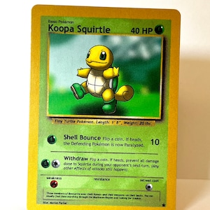 以下が含まれることがあります： ゴールドの縁取りが施されたKoopa Squirtleというタイトルのトレーディングカード。40 HPの表記があり、黄色と緑色のカメのキャラクター、Shell BounceとWithdrawという技、Tiny Turtle Pokémon、身長51cm、体重9kgというテキストが記載されています。