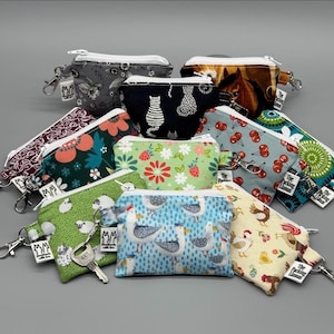 May include: A collection of small, rectangular zippered pouches featuring various fabric patterns including cats, seagulls, chickens, cherries, flowers, and horses. Each pouch has a white zipper, a metal lobster clasp, and a small white brand tag.