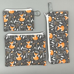 Puede incluir: Tres estuches con cremallera con estampado de zorro sobre fondo gris. Los estuches son de diferentes tama&ntilde;os y tienen cremalleras blancas. El estuche m&aacute;s grande es un estuche para l&aacute;pices, el estuche mediano es una peque&ntilde;a bolsa de maquillaje y el estuche m&aacute;s peque&ntilde;o es una cartera de monedas.