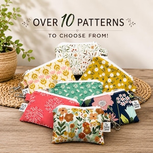 May include: A collection of small fabric zipper pouches featuring various floral and botanical patterns in colors including yellow, green, pink, and navy blue. Each pouch has a metal zipper and a small white tag labeled The Packing Llamas.